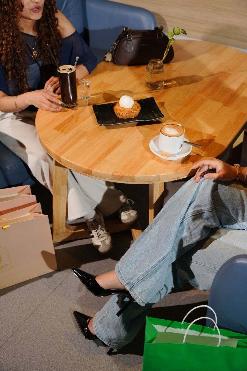 Two women at a cafe table with coffee and dessert